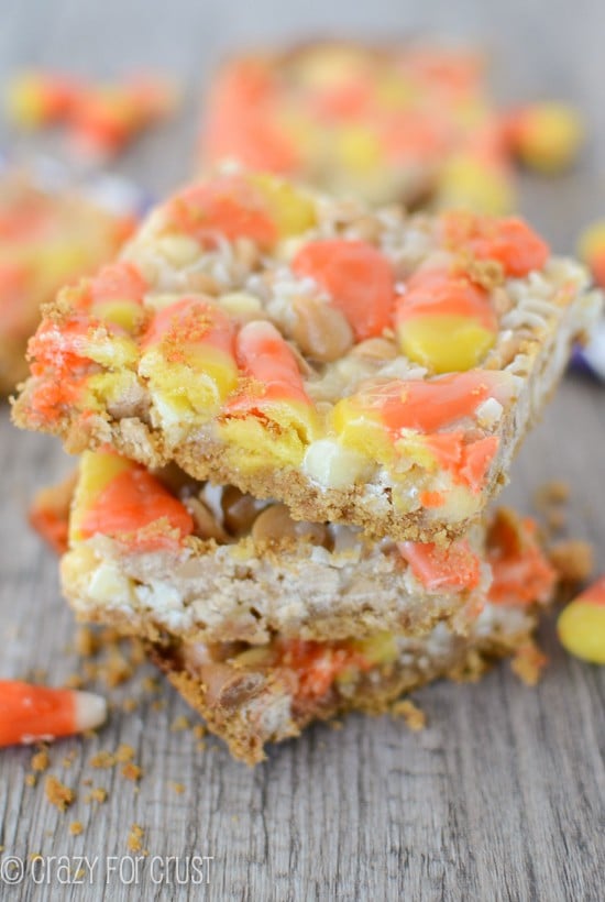 Three Candy Corn Magic Bars stacked on top of eachother with candy corn around them on a wood table