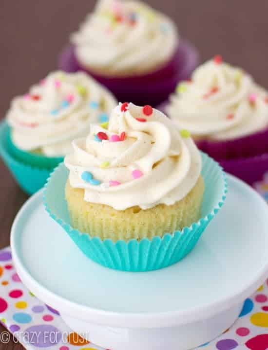 Perfect vanilla cupcakes in cupcake liners on a white pedestal.