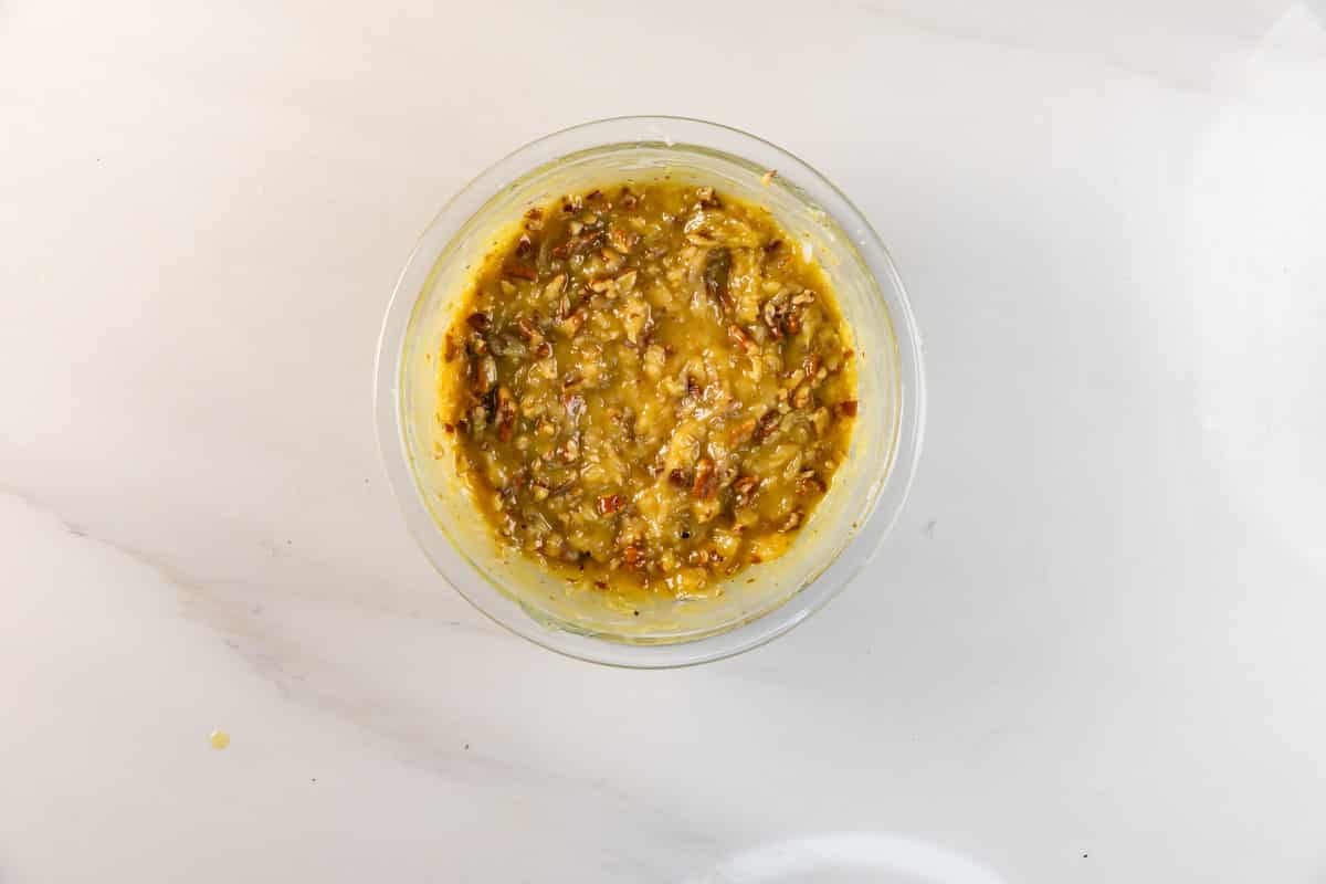 Un bol en verre rempli d'un gros mélange jaune contenant des herbes et des épices visibles, parfait pour mélanger avec des brownies au chocolat allemands, repose sur un comptoir en marbre blanc.