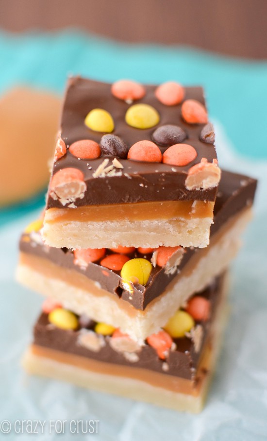 stack of cookie bars with shortbread layer, peanut butter caramel layer, chocolate layer and reese's pieces on top