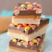 stack of cookie bars with shortbread layer, peanut butter caramel layer, chocolate layer and reese's pieces on top