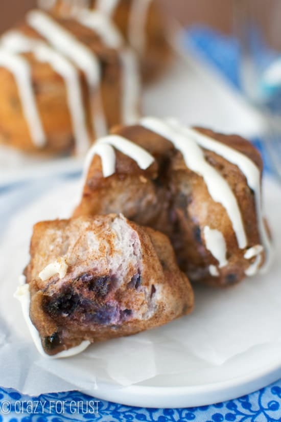 Blueberry Monkey Bread Muffin with one piece pulled off on a white plate with blue flower tablecloth underneath