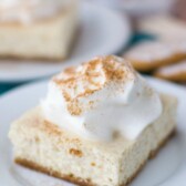 slice of cinnamon spice cheesecake bar on white plate with whipped cream