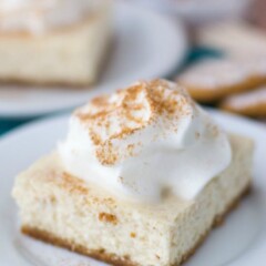 slice of cinnamon spice cheesecake bar on white plate with whipped cream