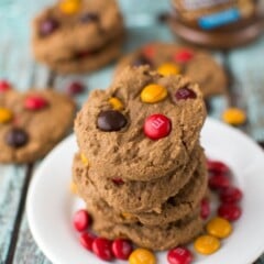 stack of dark chocolate peanut butter cookies on white plate with red and gold m and ms