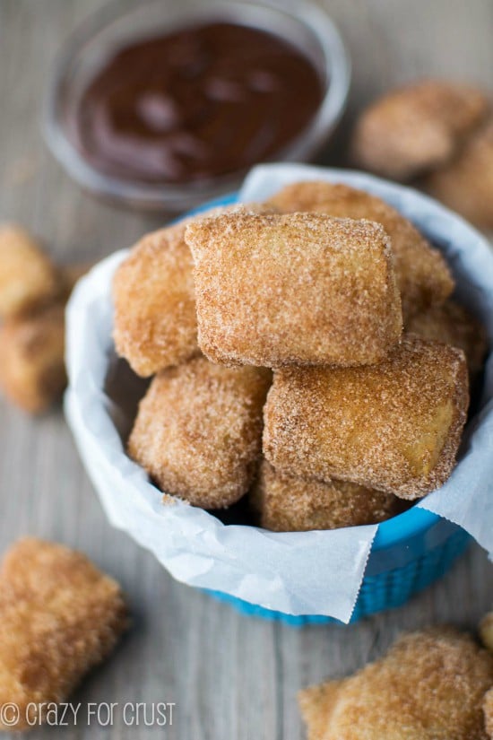 Easy Cinnamon Sugar Soft Pretzel Bites in a blue bowl with more on table and dipping sauce in background