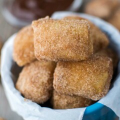 cinnamon sugar soft pretzel bites in blue dish with parchment paper and hot fudge behind