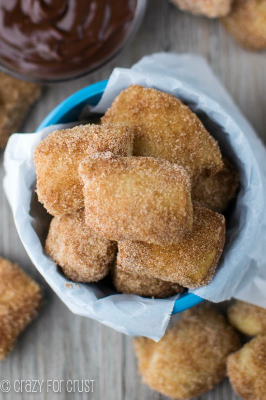 Overhead shot of Easy Cinnamon Sugar Soft Pretzel Bites in a blue bowl with more on the table and dipping sauce