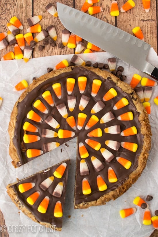 Overhead shot of Harvest Chocolate Chip Cookie Cake on white parchment paper with candy corn and knife in photo