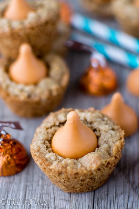 Pumpkin Spice Oatmeal Cookie Cups on a wood table with pumpkin spice hershey kisses and turquoise and white striped straws