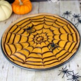 cookie pizza topped with orange frosting and spider web pattern in pizza pan on table