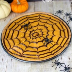 cookie pizza topped with orange frosting and spider web pattern in pizza pan on table