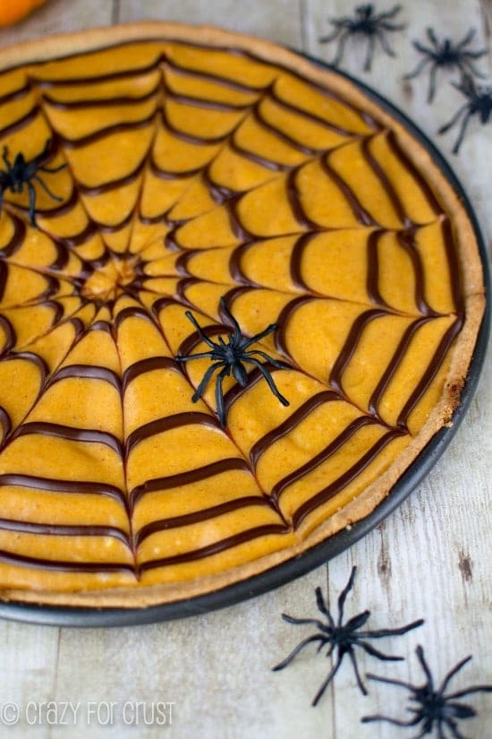 Pumpkin Spice Spiderweb Cookie Pizza on white washed wooden table with plastic spiders