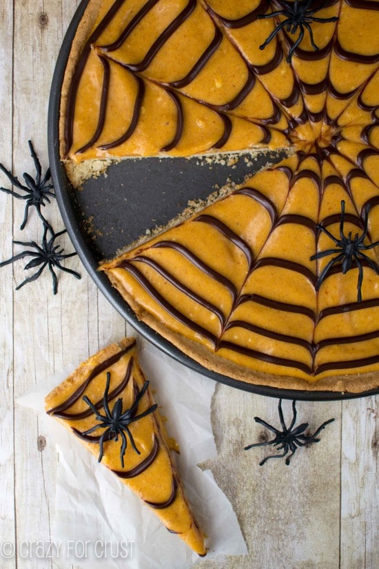 Overhead shot of Pumpkin Spice Spiderweb Cookie Pizza with one piece on the table and plastic spiders all around