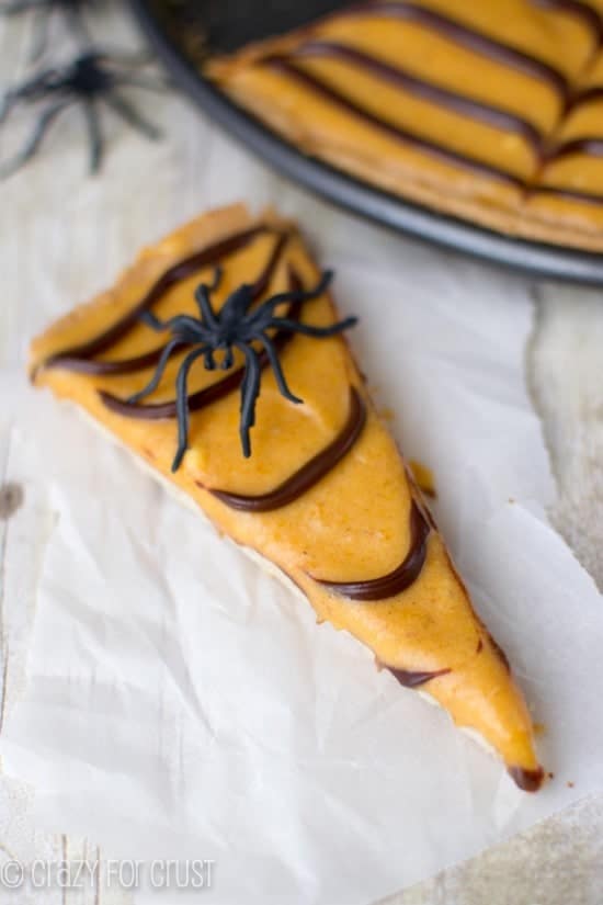 Slice of Pumpkin Spice Spiderweb Cookie Pizza on white parchment paper with a plastic spider on top
