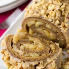 spice cake roll filled with apples and topped with caramel frosting and nuts on white platter