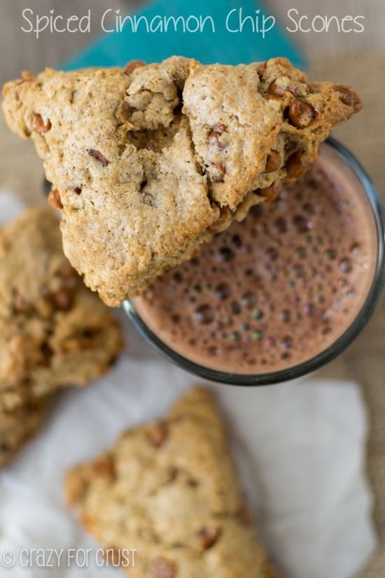 Close up shot of one Spiced Cinnamon Chip Scone sitting on top of a cup of coffee with more scones on the table