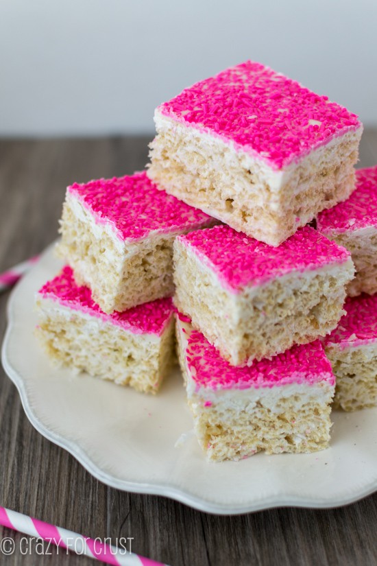 Large stack of Toasted Coconut Rice Krispie Treats with hot pink sprinkles on a white scalloped edge plate