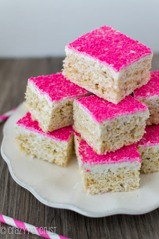 Large stack of Toasted Coconut Rice Krispie Treats with hot pink sprinkles on a white scalloped edge plate