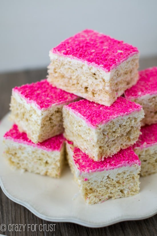 Large stack of Toasted Coconut Rice Krispie Treats with hot pink sprinkles on a white scalloped edge plate
