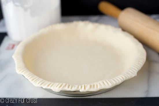 Raw All Butter Pie Crust ready to go into the oven, sitting on a silicon mat with rolling pin and flour behind it