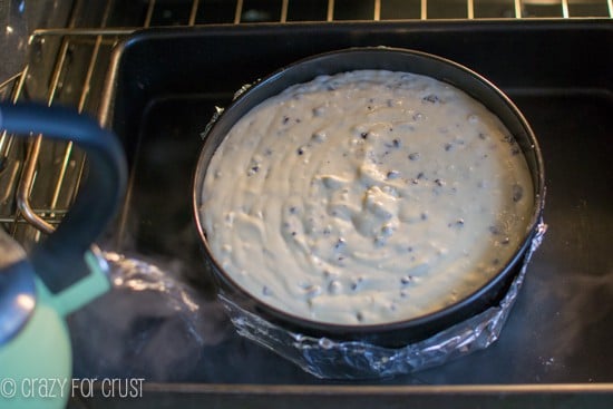 springform pan wrapped in foil in pan pouring water in for a water bath