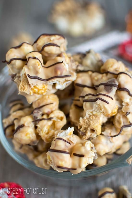 Clusters of Peanut Butter Caramel Corn with chocolate drizzle in a glass bowl