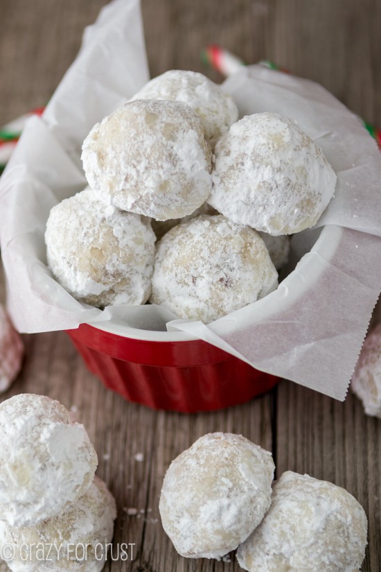 Snowball cookies in red ramekin dish with more on the wood table
