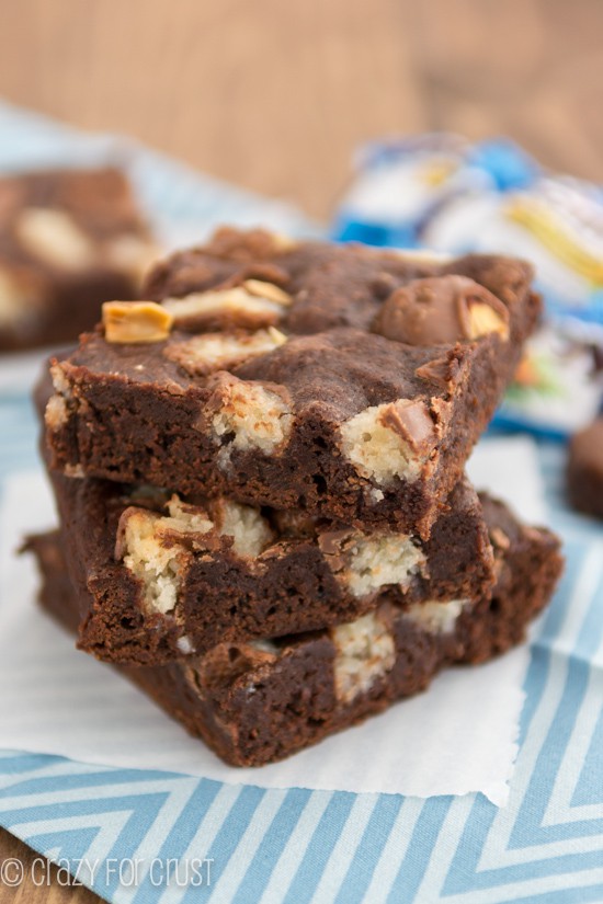 Stack of one bowl candy bar brownies with almond joy on parchment paper 