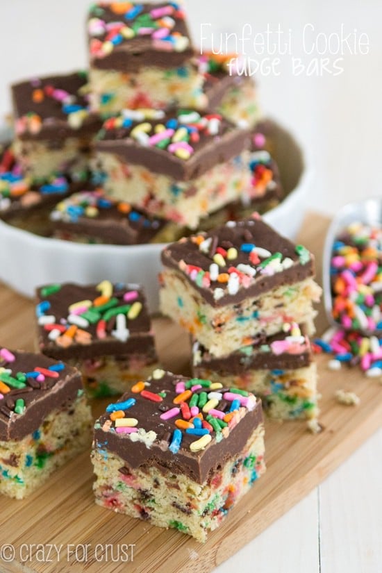 Funfetti Cookie Fudge Bars with rainbow sprinkles stacked on a wood cutting board