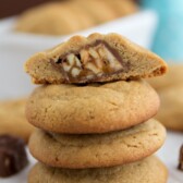 stack of peanut butter cookies with one stuffed with snickers bar cut in half on top