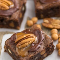 brownie with caramel and chocolate and a pecan on top on parchment paper