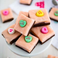 stack of pink and chocolate layered fudge with conversation hearts on white cake stand