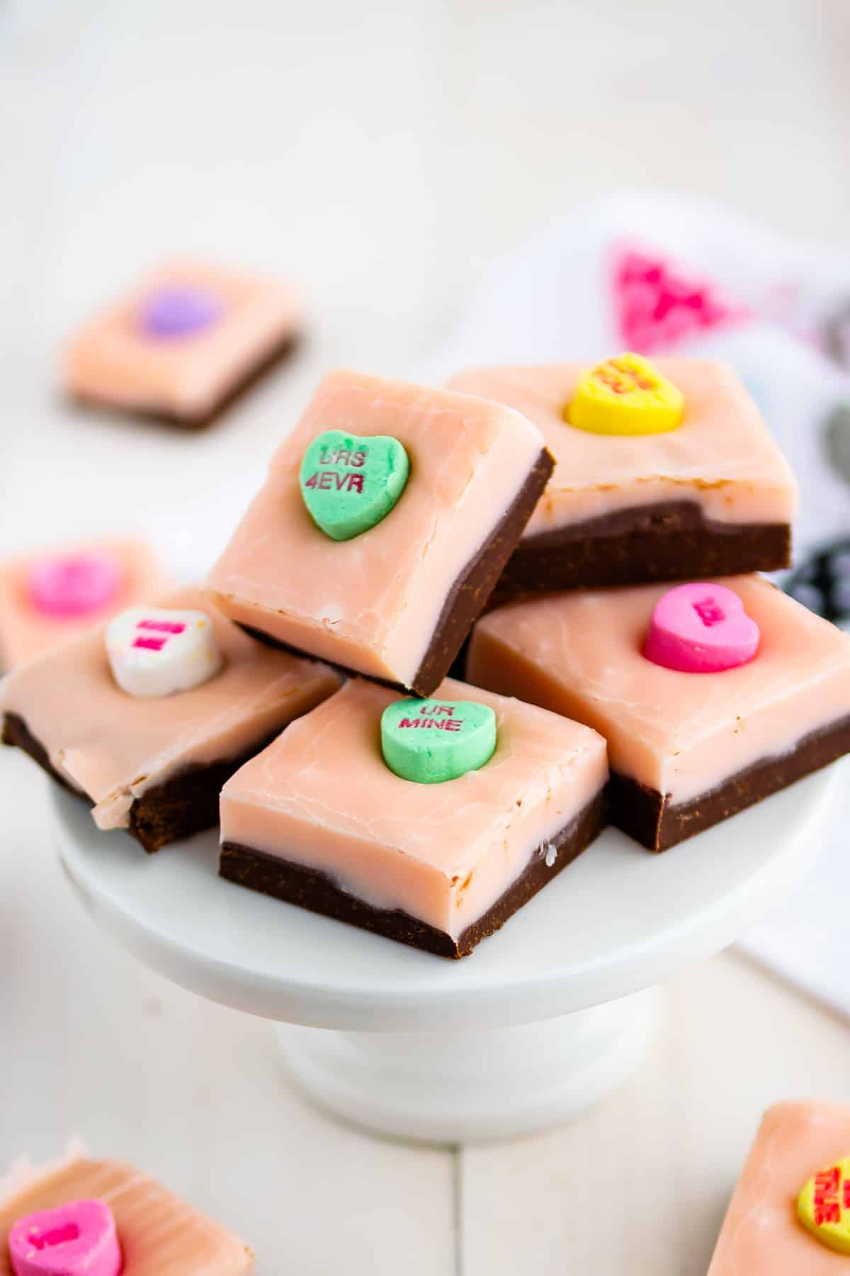 stack of pink and chocolate layered fudge with conversation hearts on white cake stand