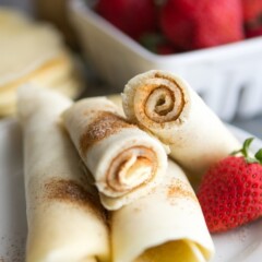 Cinnamon sugar pancake rolls on a white plate with a strawberry and more strawberries in background