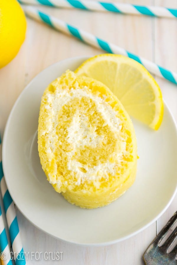 Lemon cake roll on a white serving plate with sliced lemon. 