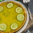 Lime Curd Pie on table with burlap, serving silverware, straws and a lime