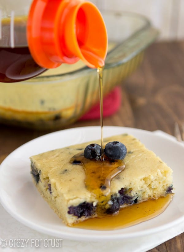 Blueberry Banana Baked Pancake on a white plate with syrup being poured on it 