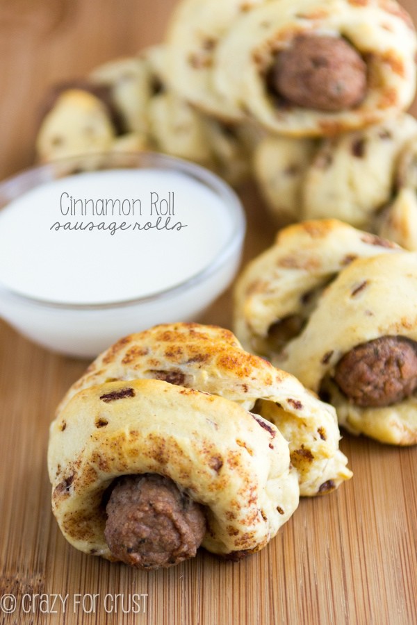 Cinnamon Roll Sausage Rolls on a wooden board with a bowl of the glaze 