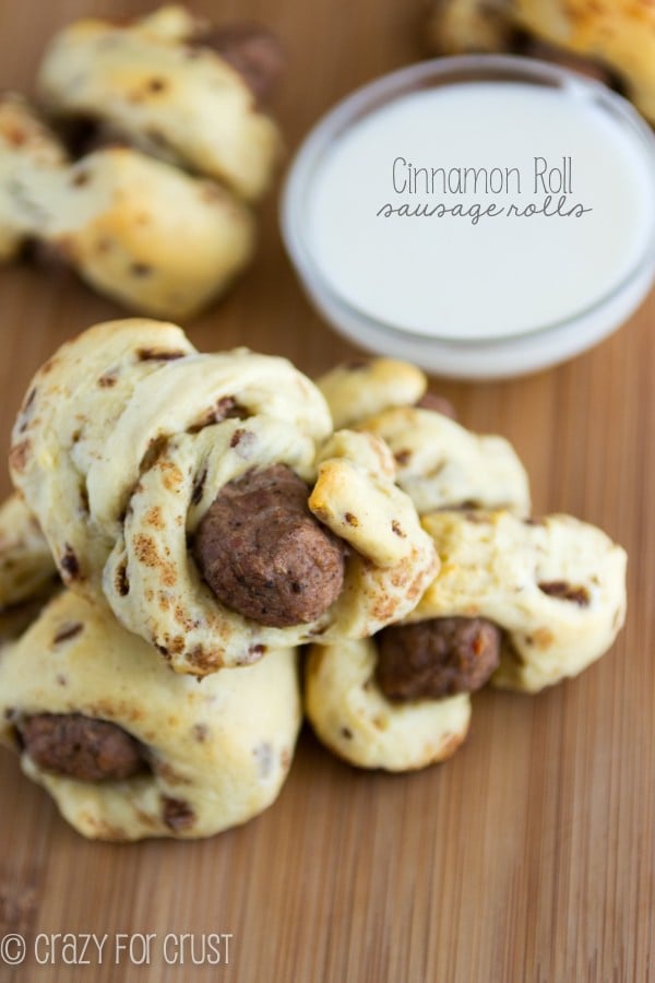  Cinnamon Roll Sausage Rolls laying on wooden board with dip in the background 