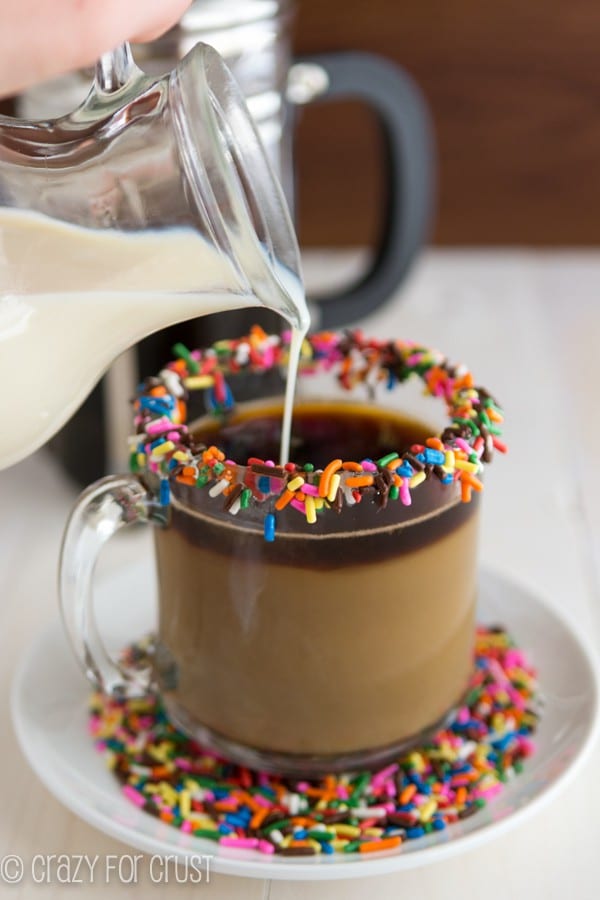 Funfetti coffee creamer poured into a coffee cup garnished with sprinkles.