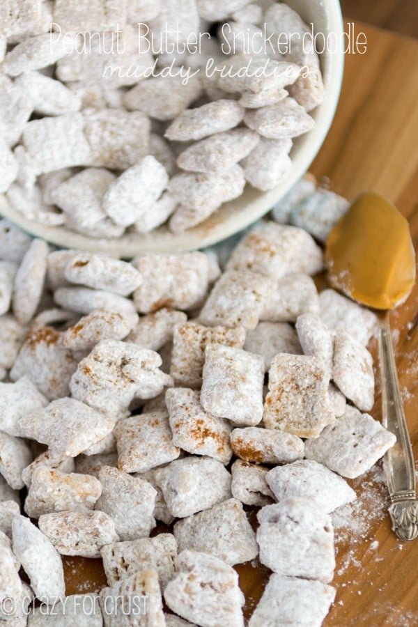 Peanut Butter Snickerdoodle Muddy Buddies sitting in a bowl and all over the table with spoonful of peanut butter laying there