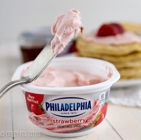 a knife scooping strawberry cream cheese out of the container 