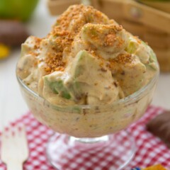 Butterfinger Apple Salad in a clear ice cream bowl sitting on top of a red checkered towel