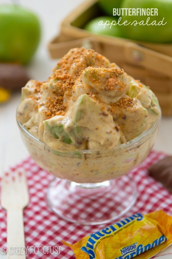 Butterfinger Apple Salad in a clear ice cream bowl sitting on top of a red checkered towel