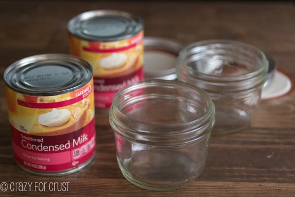 2 mini clear Mason jars next two 2 cans of Sweetened Condensed Milk on a wooden board 