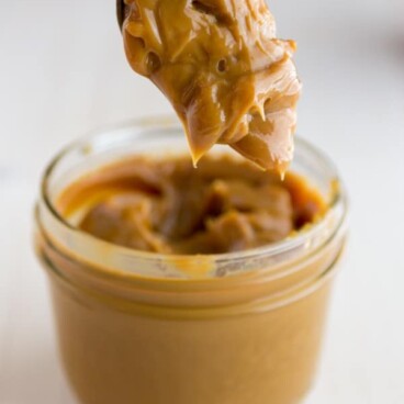 A spoon scooping the Homemade Crockpot Dulce de Leche out of a small clear cup