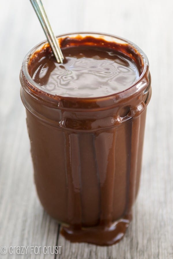 Thick homemade chocolate sauce in jar with a spoon.