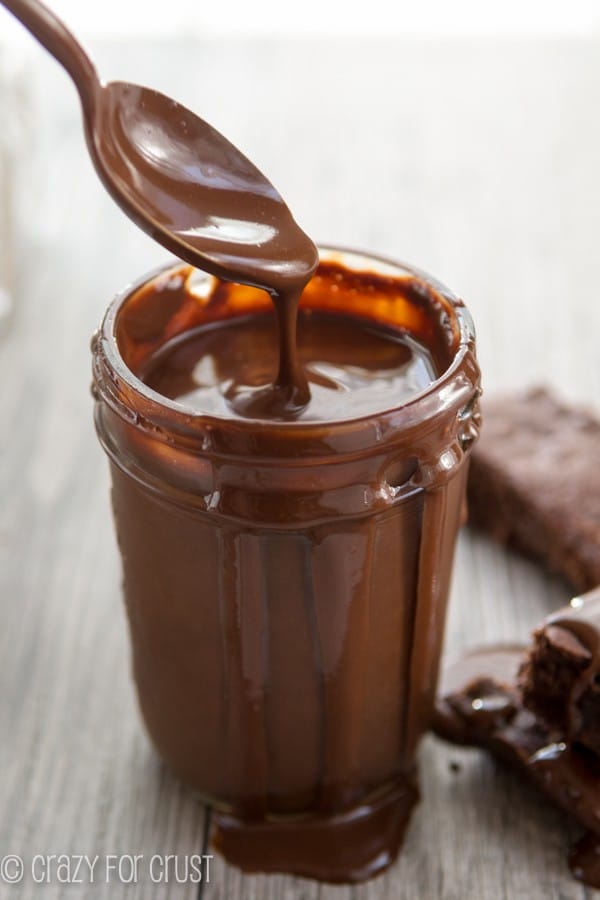 Chocolate Sauce in clear jar with a spoon scooping it out 