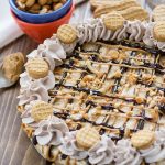 This No-Bake Frozen Peanut Butter Cheesecake on a brown board with blue and orange bowl with nuts in them